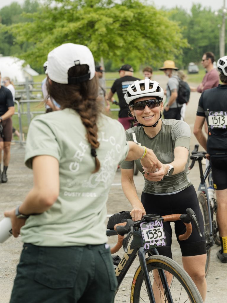 Bénévole qui remet une bière À L'Abordgae à une cycliste à Gravelooza